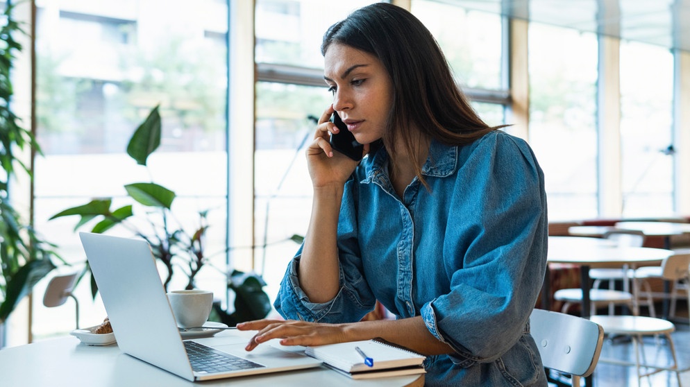 Junge Frau telefoniert und arbeitet gleichzeitig am Laptop. Wenn ihr beim Arbeiten ständig unterbrochen werdet, zwischen verschiedenen Aufgaben wechselt und alles gleichzeitig erledigen wollt, solltet ihr aufpassen. Multitasking kann sogar zu Burnout und Depressionen führen.  | Bild: picture alliance / Westend61 | NOVELLIMAGE